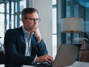 Mann vor dem Laptop wartet, da Outlook langsam lädt und seine Produktivität beeinträchtigt.