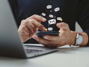 Person nutzt Smartphone zum Senden und Empfangen von E-Mails, Symbole für Nachrichten schweben über dem Gerät, moderner digitaler Kommunikation im Büro