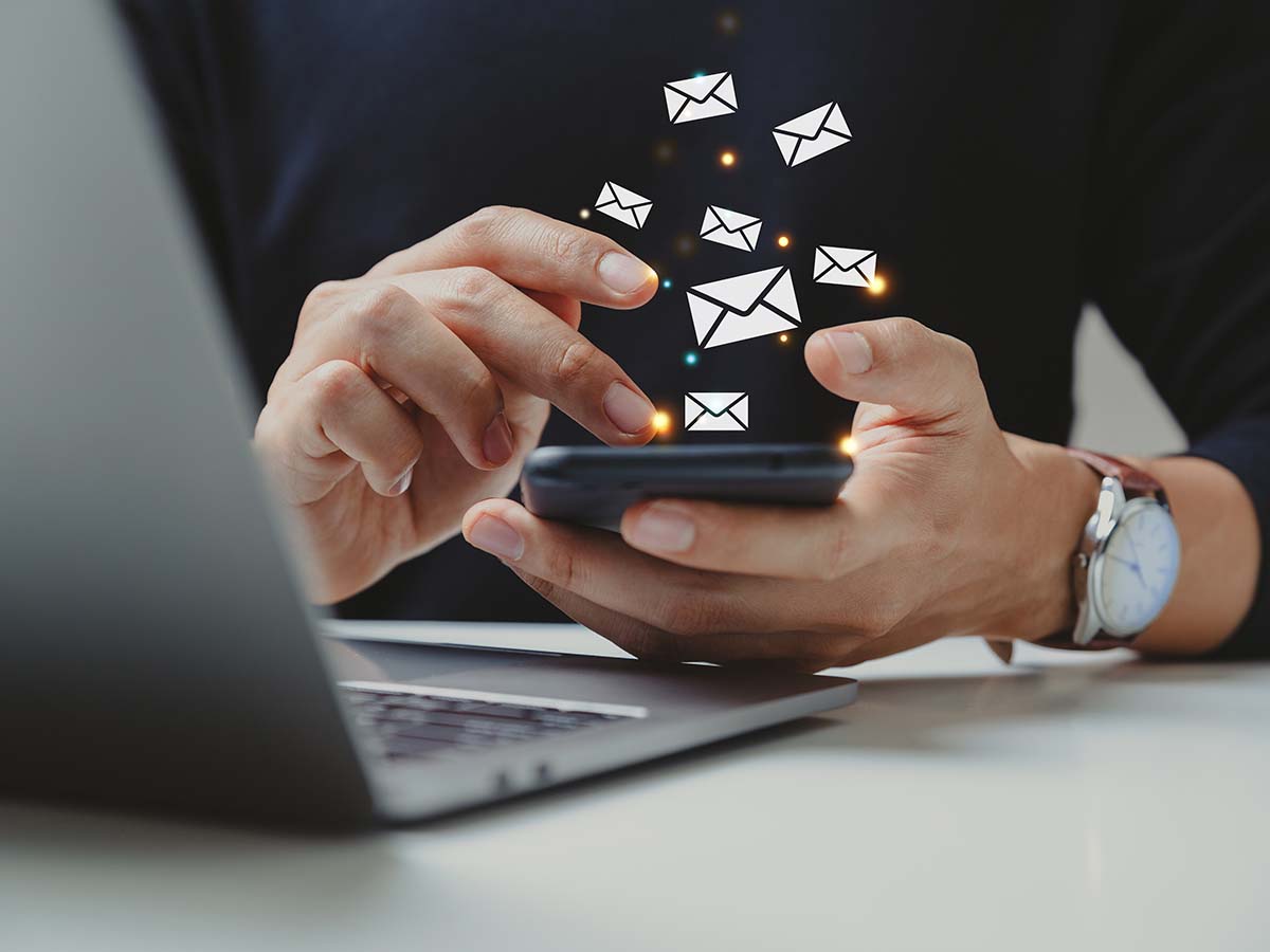 Person nutzt Smartphone zum Senden und Empfangen von E-Mails, Symbole für Nachrichten schweben über dem Gerät, moderner digitaler Kommunikation im Büro