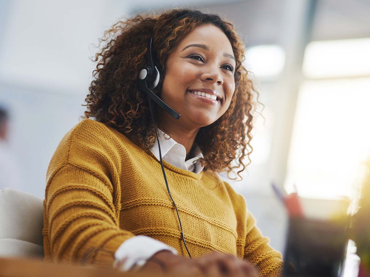 Freundliche IT-Support-Mitarbeiterin mit Headset am Computer für Remote Desktop Fernwartung und Online-Hilfe.